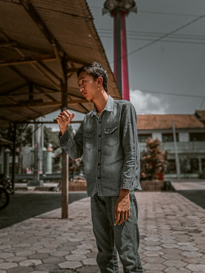 Young man looking away while standing on footpath