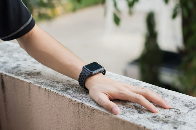 Cropped hand of man wearing smart watch on retaining wall