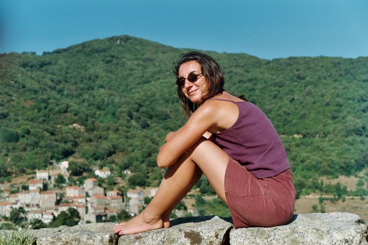 Woman wearing sunglasses looking away while sitting against mountains
