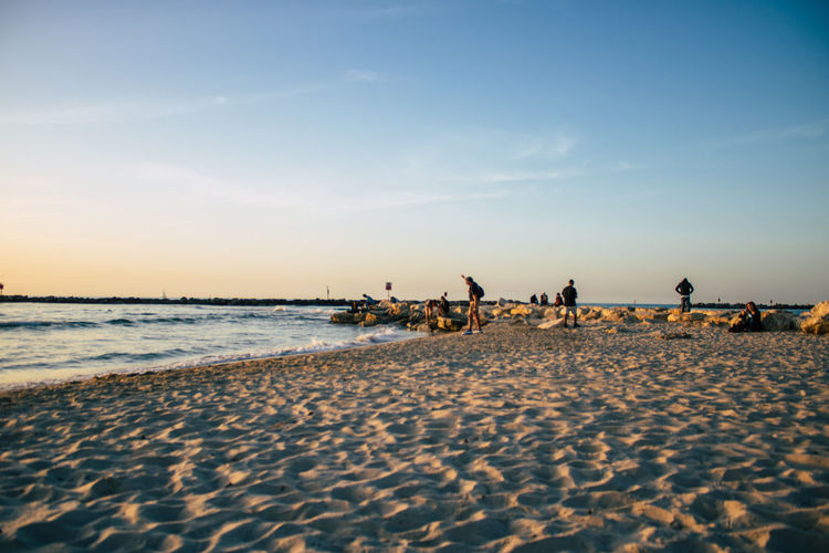 People relaxing on beach against sky during sunset