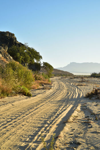 Road leading towards mountains against clear sky