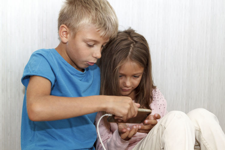 Kids playing with mobile phone while sitting in bedroom