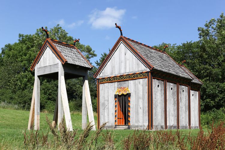 Wooden house on field by trees against sky