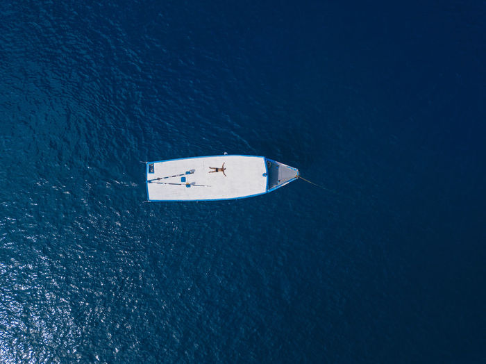 Aerial view of shirtless man relaxing on roof of boat drifting in blue waters of arabian sea in summer