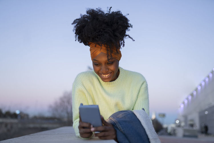 portrait of young woman using mobile phone against clear sky