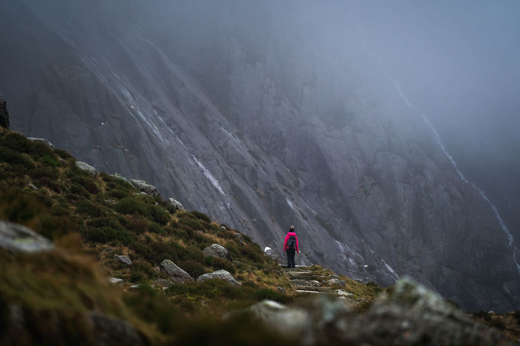 Rear view of person standing on rock against mountains