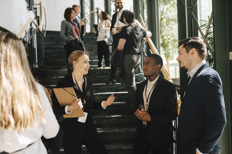 Female entrepreneur discussing with male colleagues while standing by staircase at convention center