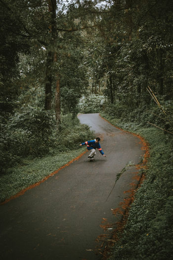 Man skateboarding on road amidst trees