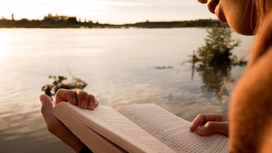 Midsection of woman reading book against lake