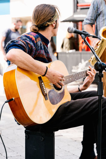Man with tied long hair singing and playing a guitar in the street