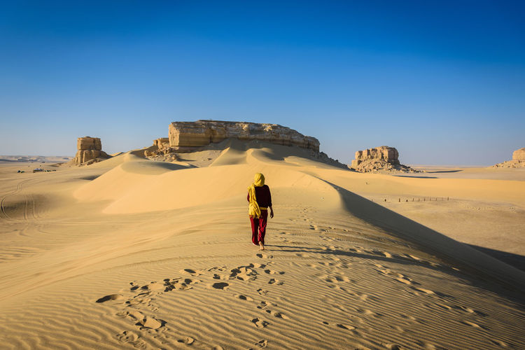 Woman walking on sand dune in desert against clear sky