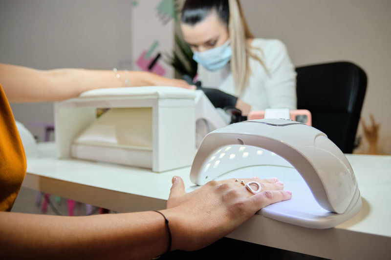 Crop anonymous female customer putting hand on uv lamp for drying nails while getting professional manicure in modern salon
