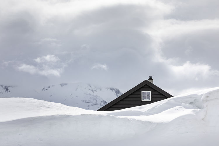 Snow covered house by building against sky