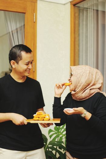 A husband and wife eat risoles standing at home