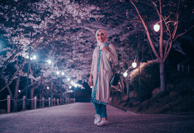 Portrait of woman standing against illuminated trees at night