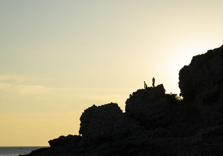 Silhouette rocks on cliff by sea against sky during sunset