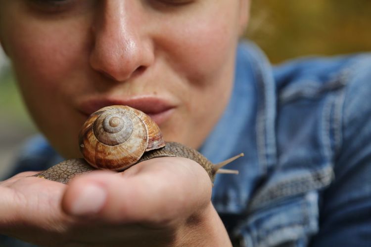 Cropped image of woman kissing snail on palm