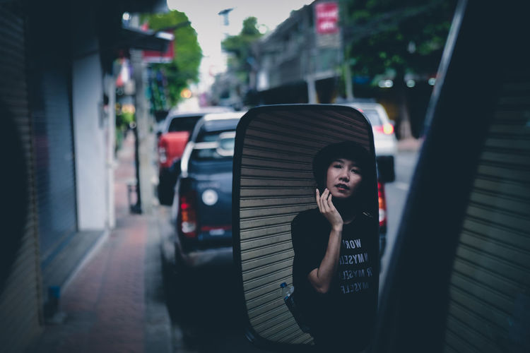 Reflection of young woman in side view mirror of car on street