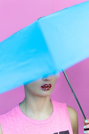 Woman with chocolate sprinkles on lips holding umbrella against pink background