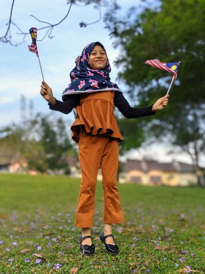 Full length of girl standing on grass and holding malaysian flag called jalur gemilang