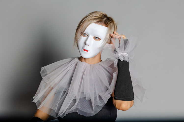 Woman in white theater mask and harlequin collar on gray background. fancy dress, masquerade clothes