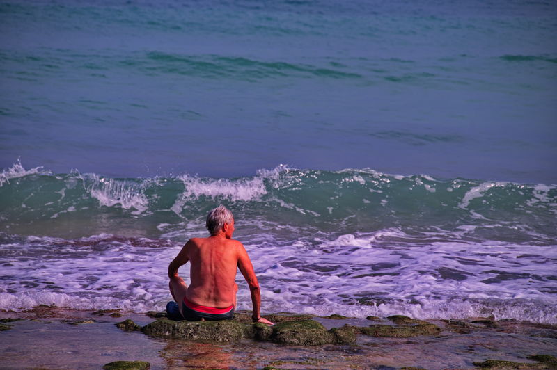Senior man sitting on sandy beach near blue ocean