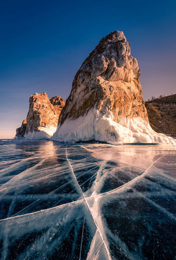 Scenic view of frozen sea by rock formation against blue sky