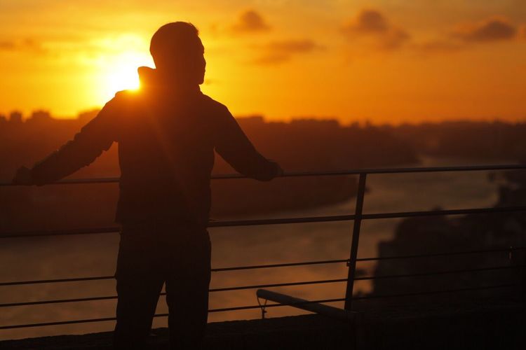 Silhouette man with arms raised against sunset sky