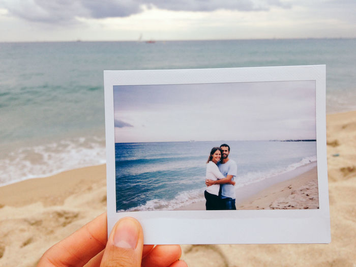Cropped hand of person holding couple photograph at beach