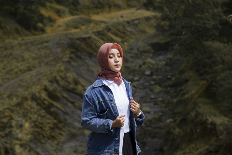 Asian muslim  young woman shut her eyes  while standing outdoors at kali talang, yogyakarta