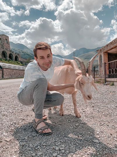 Portrait of man crouching with goat on land against sky