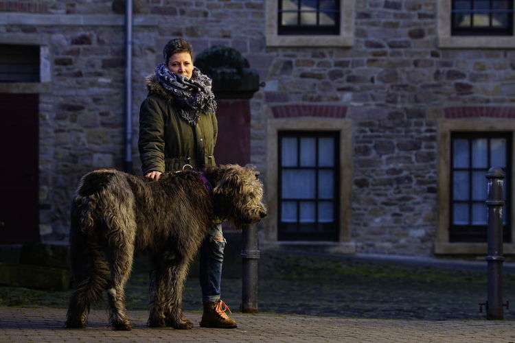 Full length portrait of woman with irish wolfhound on footpath against building