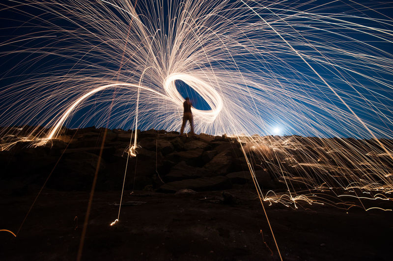 Low angle view of man spinning wire wool against sky at night