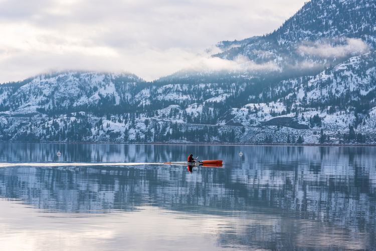 Person paddles  a kayak across skaha lake during the calm after a winter storm. 