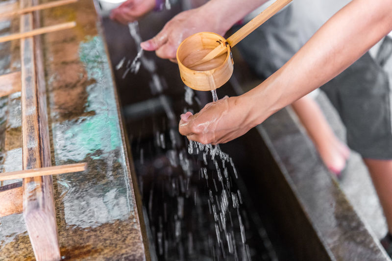 Cropped image of woman washing hand with wooden ladle at temple