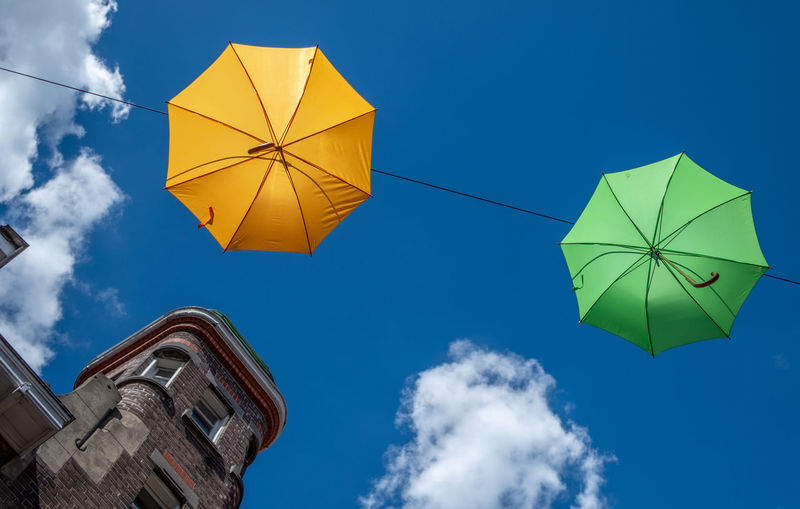 Low angle view of umbrellas hanging by building against blue sky