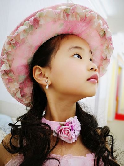 Close-up of cute girl wearing hat looking away while standing against wall