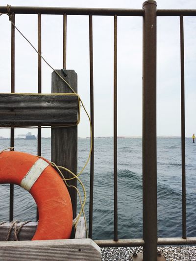 Orange life belt by railing against sea