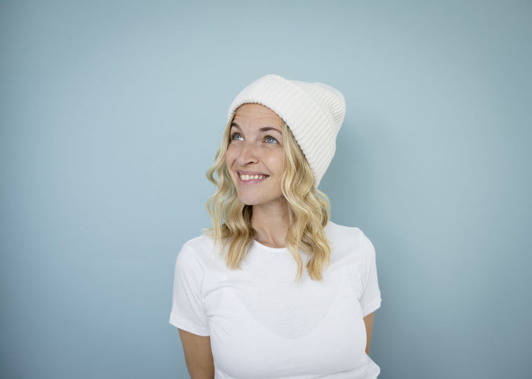 Portrait of smiling young woman wearing hat against blue background