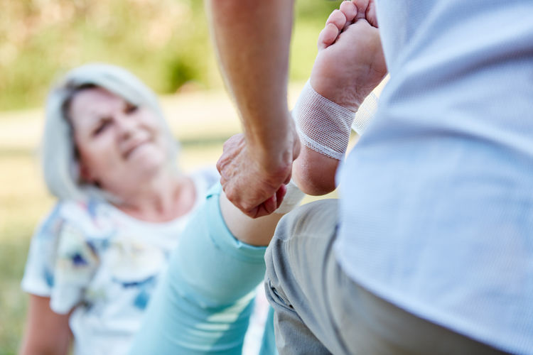 Midsection of man applying bandage to senior woman
