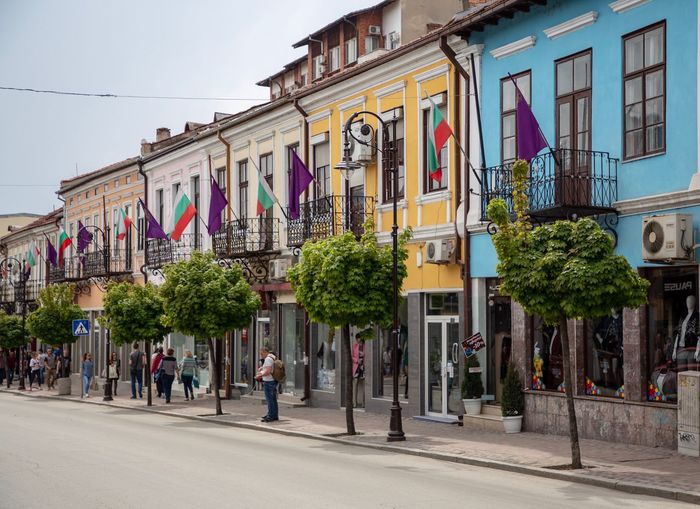 People on street by buildings in city against sky