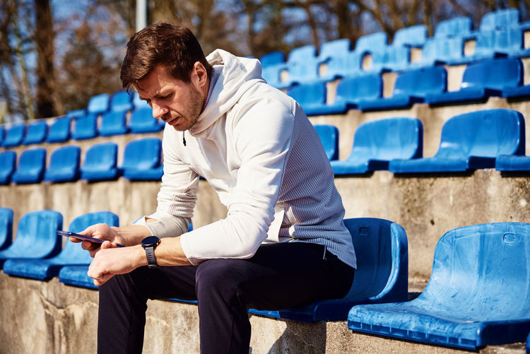 Man in sportswear sitting on stadium seat and browsing smartphone