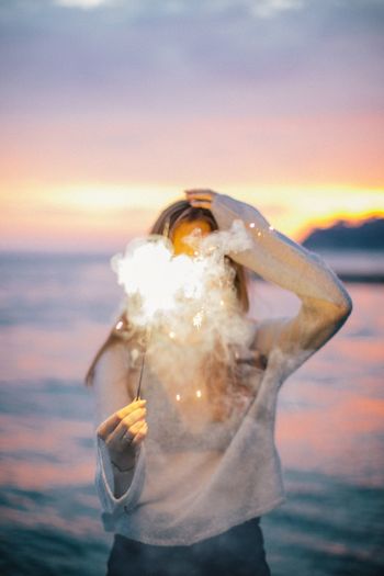 Woman with lit sparkler standing at beach during sunset