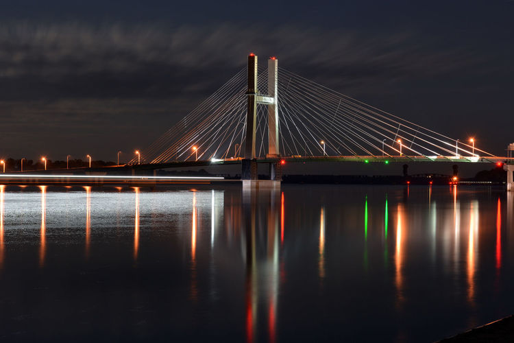 Illuminated cable-stayed bridge over river against sky at night