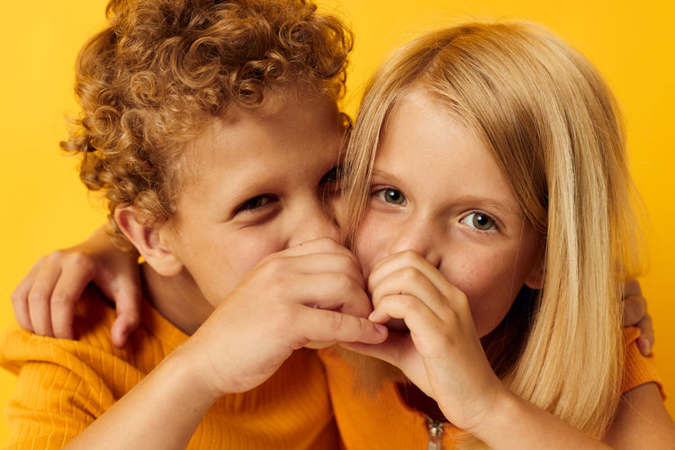 Cute sibling whispering against yellow background