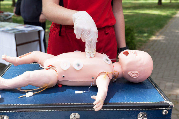Midsection of rescue worker performing cpr on baby mannequin