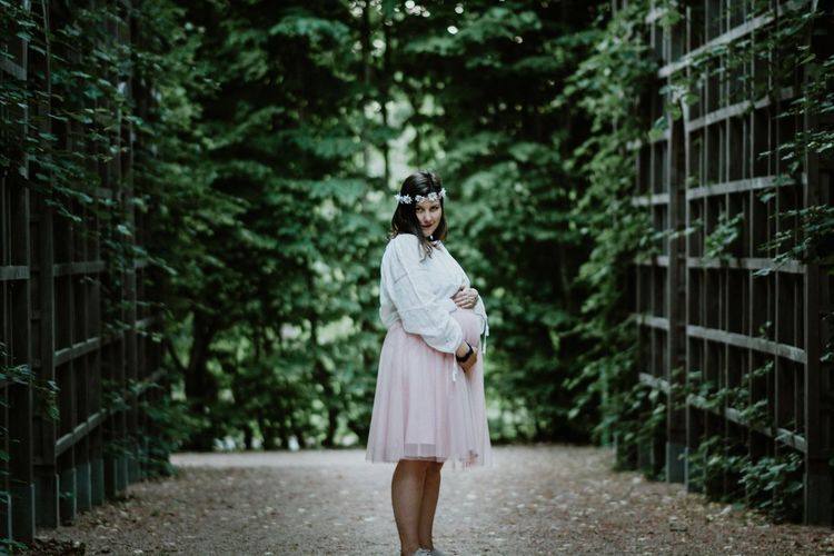 Portrait of pregnant woman standing against trees