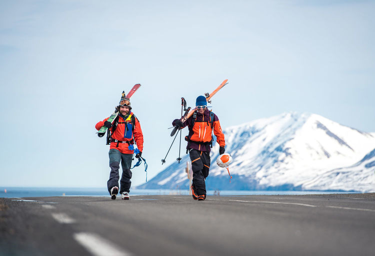 Two men walking with skis on a paved road in iceland with mountains