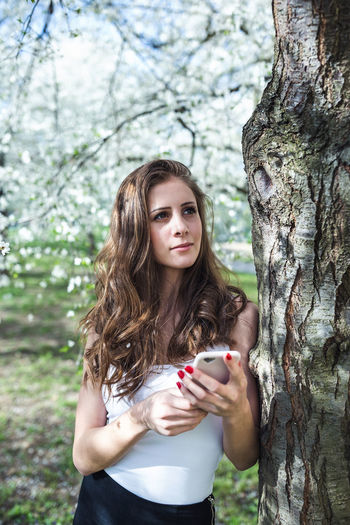 Young woman with a smart phone under the blooming trees in park. spring season 