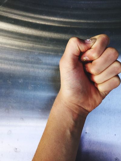 Cropped hand of woman clenching fist against metal